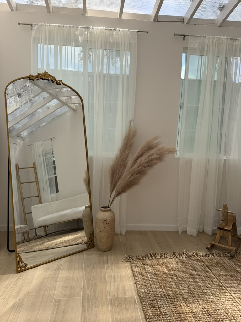 Memory Bloom Cottage interior with ornate gold-framed mirror, sheer curtains, pampas grass in ceramic vase, and natural wood floors